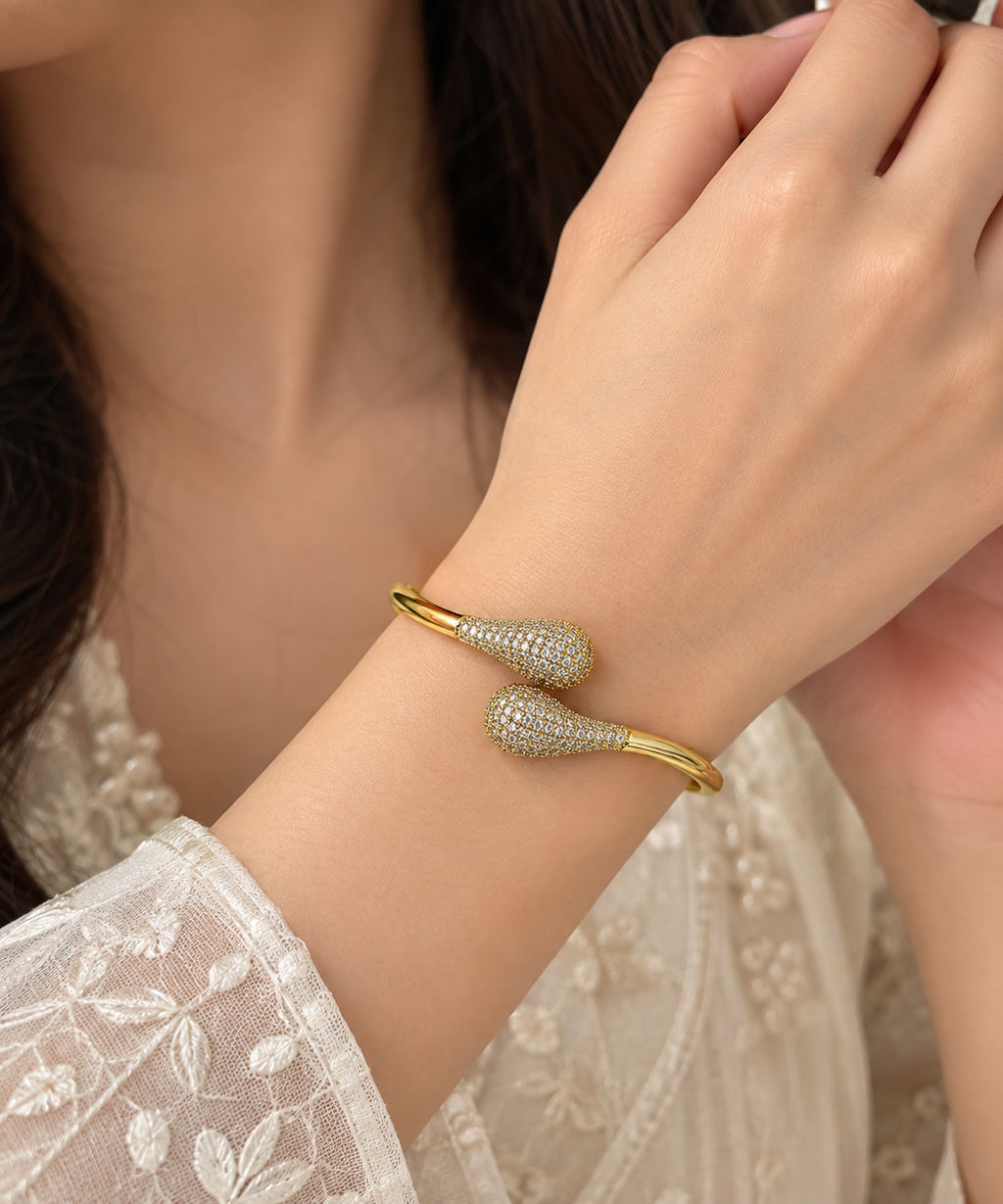 Anti tarnish ,this elegant Gold Tone Crystal Pave Open Cuff Bangle. Designed with a sleek open-cuff silhouette and beautifully detailed teardrop-shaped ends, this statement bracelet combines a polished gold-tone finish with sparkling crystal-style stone